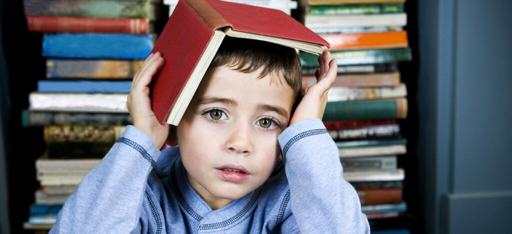 little boy struggling to read, holding book on his head
